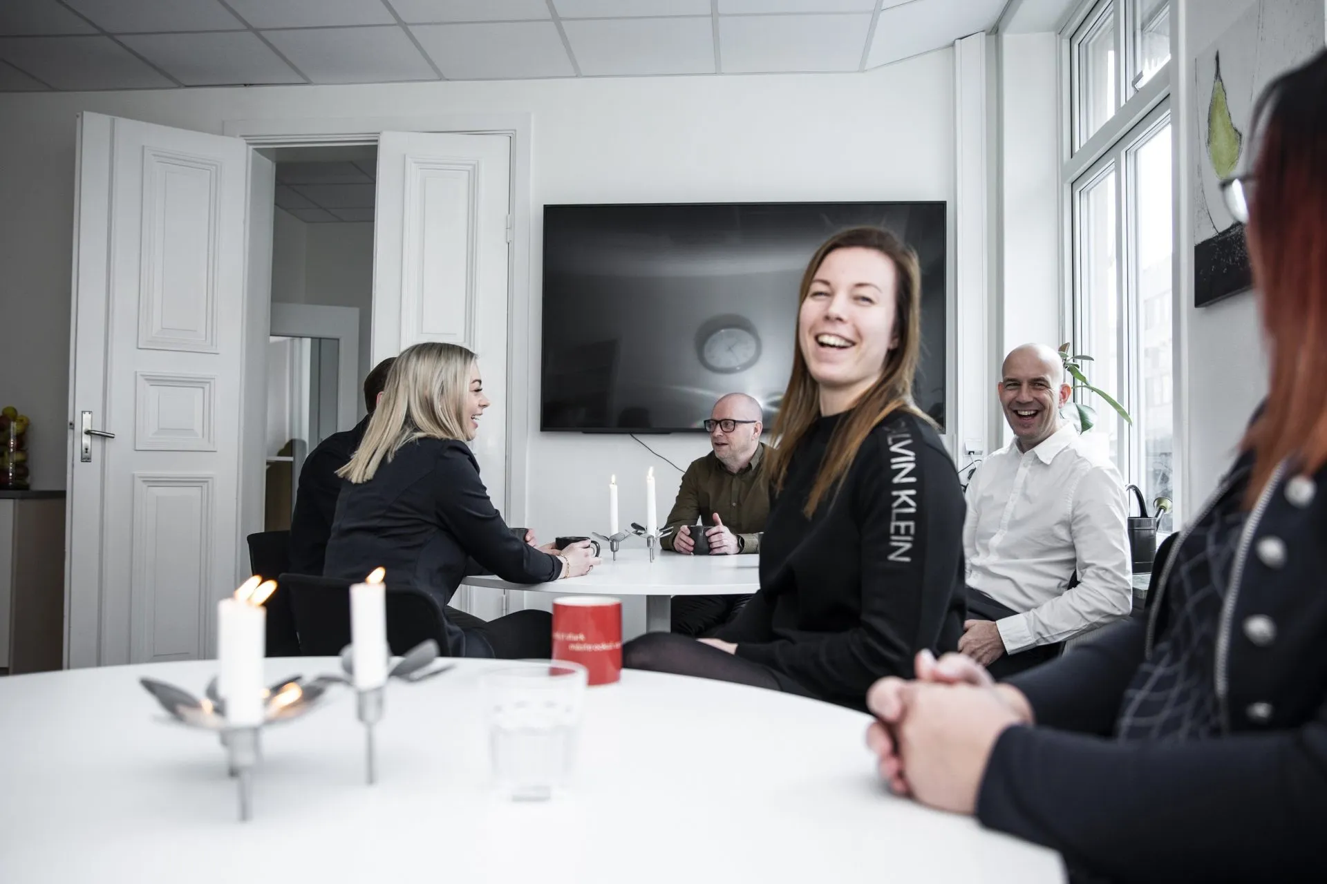 En grupp med sex glada medarbetare som sitter vid fikabord.