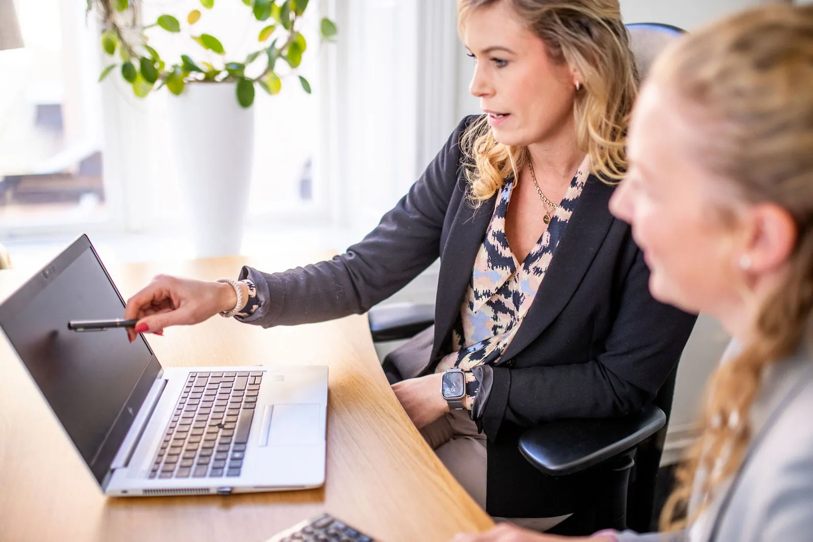 En kvinna pekar på en bärbar dator. En annan kvinna sitter bredvid och tittar på.