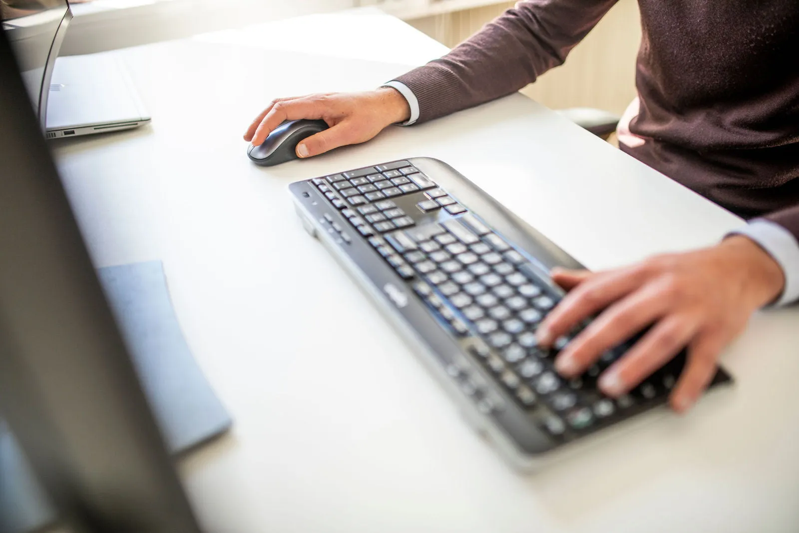 Ett tangentbord på ett skrivbord. Fokus är på händerna som skriver på det.