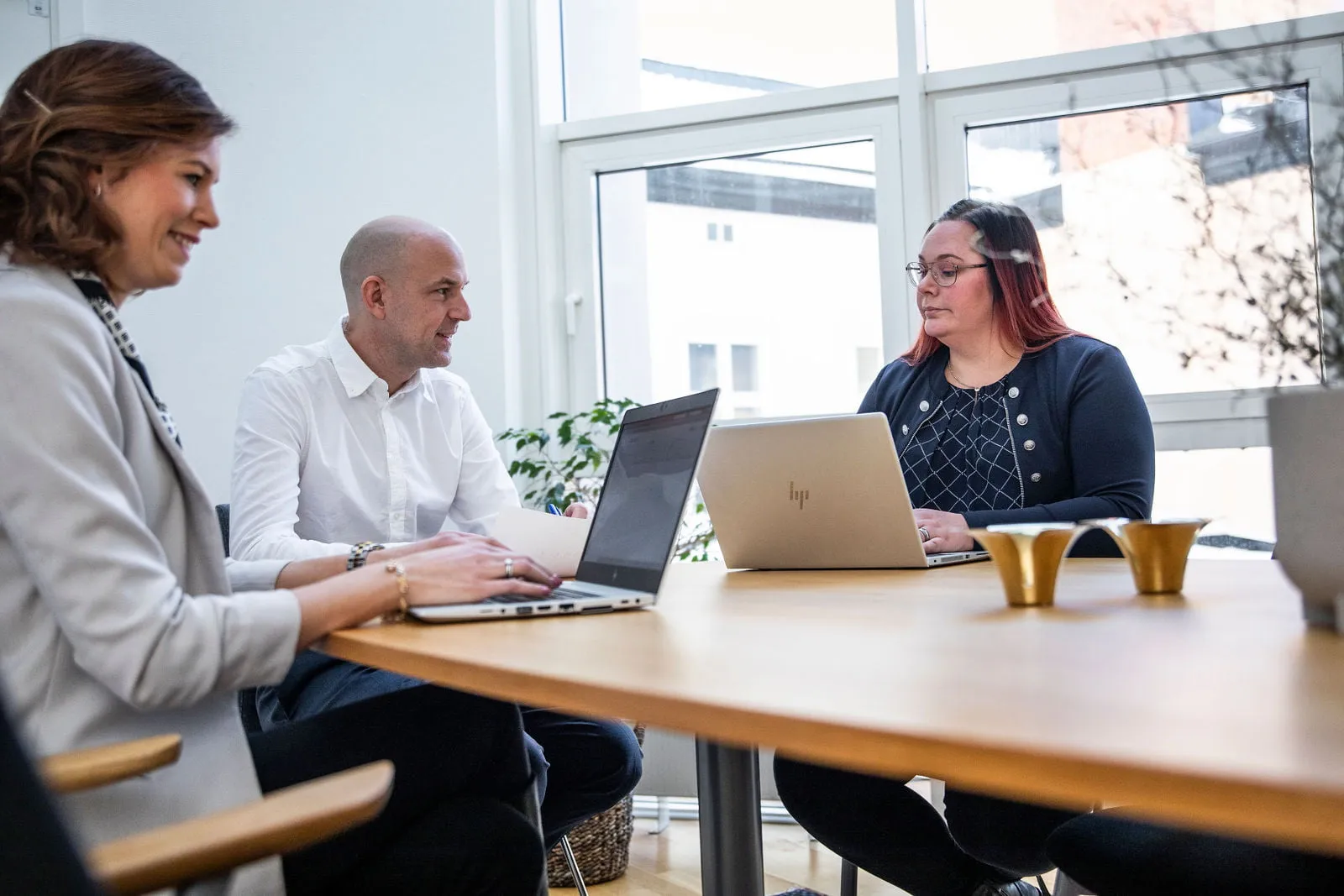 Två kvinnor och en man sitter i ett konferensrum med bärbara datorer framför sig. De är glada.