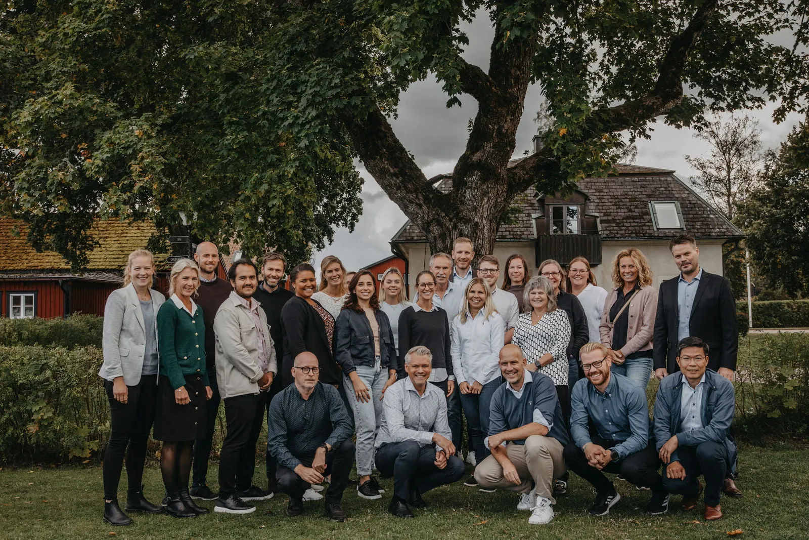 En gruppbild med alla medarbetarna står i en trädgård framför ett stort träd.